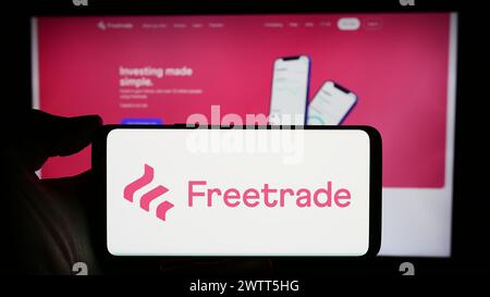 Person, die ein Mobiltelefon mit dem Logo der britischen Fintech-Firma Freetrade Ltd. Vor der Webseite hält. Schwerpunkt auf dem Display des Telefons. Stockfoto