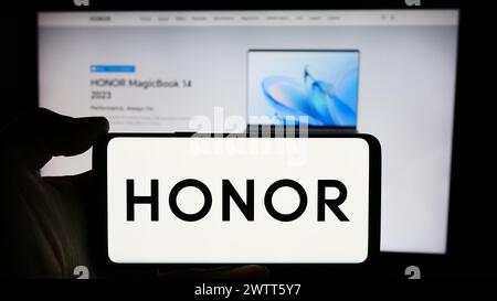 Person, die ein Mobiltelefon mit dem Logo des chinesischen Smartphone-Unternehmens Honor Device Co. Ltd. Vor der Webseite des Unternehmens hält. Schwerpunkt auf dem Display des Telefons. Stockfoto