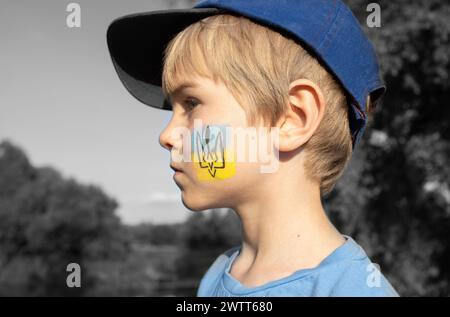 Junge mit nationalem Symbol auf der Wange - Dreizack auf blaugelbem Hintergrund. Ukrainisches patriotisches Konzept Stockfoto