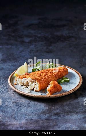 Knuspriger panierter Fisch, serviert mit einem Keil frischer Zitrone auf einem rustikalen Teller. Stockfoto