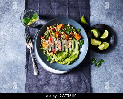 Ein lebhaftes grünes Avocadopüree mit einem farbenfrohen Quinoa-Salat auf einem stilvollen Teller. Stockfoto