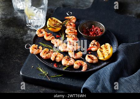 Gegrillte Garnelenspieße mit Zitrone und Dippsoße auf einem dunklen, rustikalen Tisch. Stockfoto