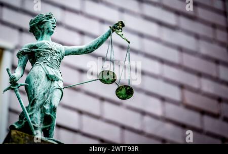 Eine verwitterte Statue von Lady Justice, die die Waage der Gerechtigkeit vor einer verschwommenen Gebäudekulisse hält. Stockfoto