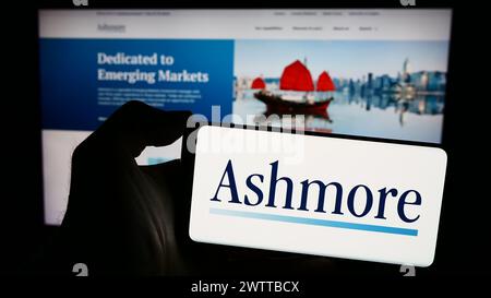 Person, die ein Smartphone mit dem Logo der britischen Investmentmanagementgesellschaft Ashmore Group plc vor der Website hält. Schwerpunkt auf dem Display des Telefons. Stockfoto