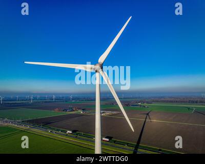 Eine majestätische Windenergieanlage steht hoch vor einem klaren blauen Himmel mit Blick auf eine grüne Landschaft Stockfoto