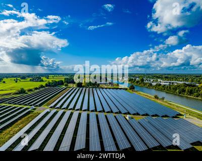 Ein grandioser Blick auf einen Solarpark neben einem Fluss unter dem riesigen, wolkengestreuten Himmel. Stockfoto