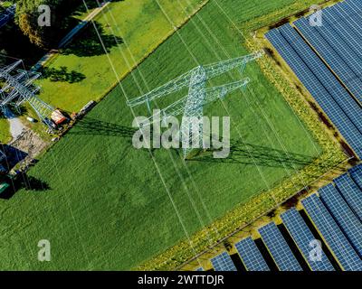 Blick aus der Vogelperspektive auf Solarpaneele neben einem Strommast auf üppig grünen Feldern Stockfoto