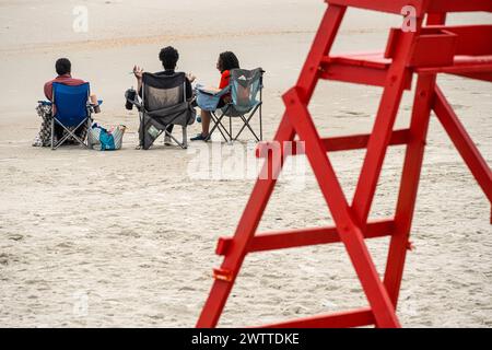 Drei Frauen, die bei Sonnenaufgang am Strand in Jacksonville Beach, Florida, eine entspannende Diskussion führen. (USA) Stockfoto