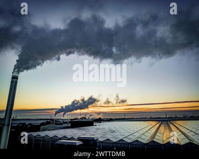 Industrieller Sonnenuntergang mit Schornsteinen, die sich vor einem lebendigen Himmel abzeichnen Stockfoto
