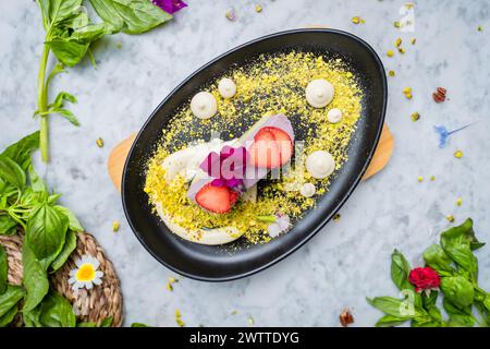 Ein Teller mit veganem Blaubeeren-Matcha-Kuchen mit Erdbeeren auf der Seite Pistazien. Serviert auf einem Teller mit Früchten. Stockfoto