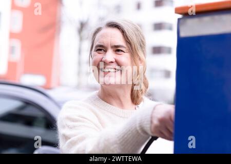Frau, die ihr Elektroauto auflädt Stockfoto