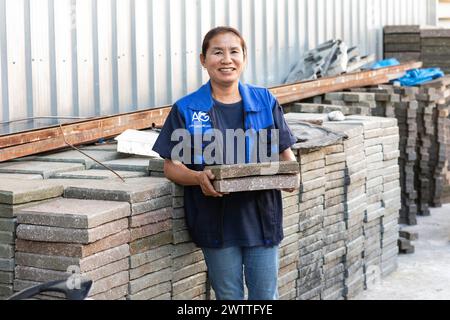 Ein lächelnder Arbeiter, der Ziegeln in einer Plastikrecyclingfabrik in Thailand hält Stockfoto