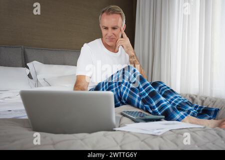 Mann mit Laptop, der auf einem Bett sitzt Stockfoto