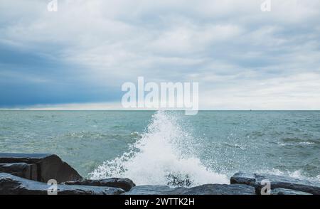 Stürmische Meereswellen stürzen unter bewölktem Himmel gegen die zerklüftete felsige Küste Stockfoto