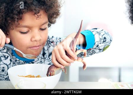 Kind, das beim Frühstück mit einem Spielzeug-Dinosaurier spielt Stockfoto