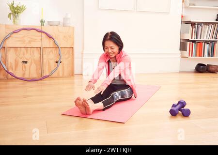 Frau, die sich zu Hause auf einer Yogamatte ausdehnt Stockfoto