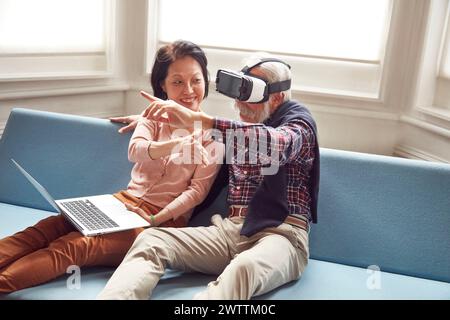 Älteres Paar mit VR-Headset und Laptop auf dem Sofa Stockfoto