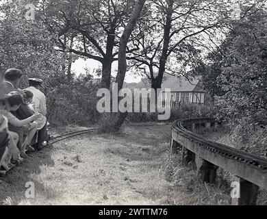 1960er Jahre, historisch, sommerlich und Menschen, die eine Fahrt mit einer Miniaturbahn genießen, Zugführer mit Hut, der die Miniatur-Dampfeisenbahn fährt, England, Großbritannien. Stockfoto