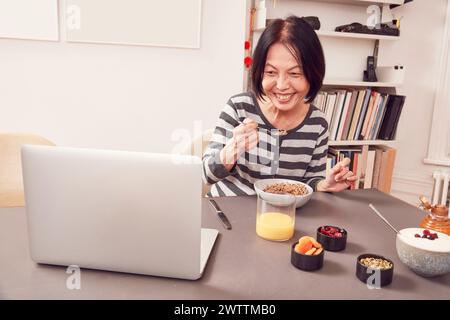 Frau frühstückt, während sie an einem Laptop arbeitet. Stockfoto