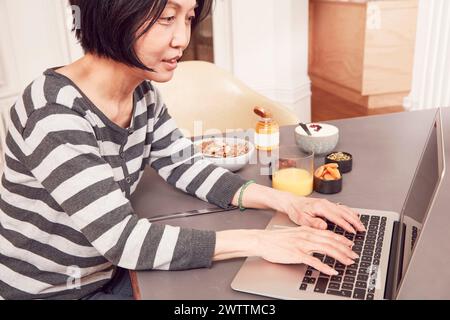 Frau, die am Laptop arbeitet und in der Nähe frühstückt Stockfoto