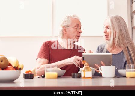 Älteres Ehepaar, das ein Tablet am Frühstückstisch benutzt Stockfoto