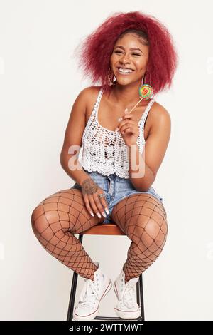 Woman with red hair sitting on stool holding a lollipop Stockfoto