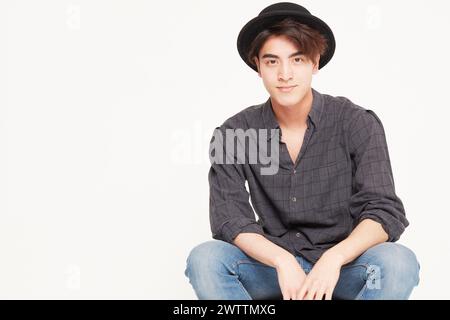 Junger Mann mit Hut, der beiläufig sitzt Stockfoto