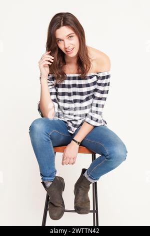 Frau, die auf einem Hocker sitzt, in lässiger Kleidung Stockfoto