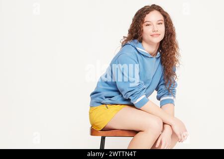 Frau, die auf einem Hocker sitzt, in blauem Sweatshirt und gelben Shorts Stockfoto