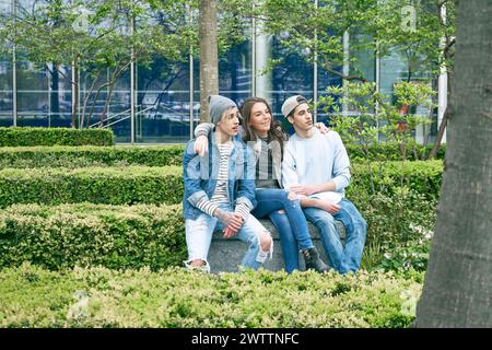 Drei Freunde sitzen und posieren in einem grünen Stadtpark Stockfoto