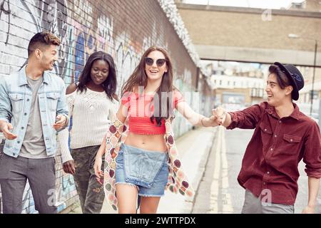 Freunde laufen und lachen zusammen in einer mit Graffiti bedeckten Gasse. Stockfoto
