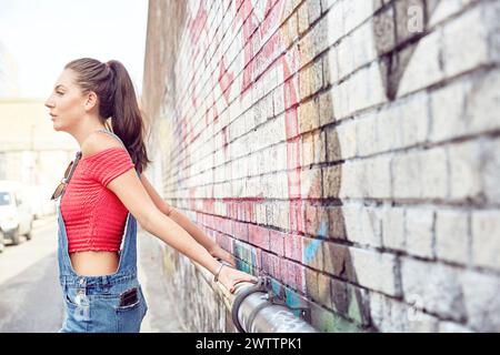 Frau, die sich an einem Geländer an einer Graffiti-Wand lehnt Stockfoto