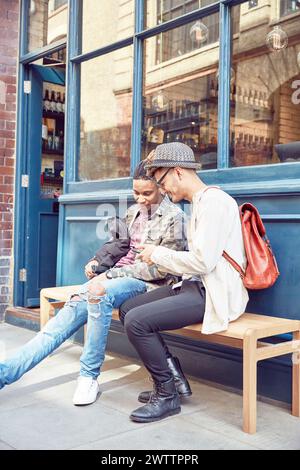 Zwei Personen sitzen auf einer Bank und schauen auf ein Smartphone Stockfoto