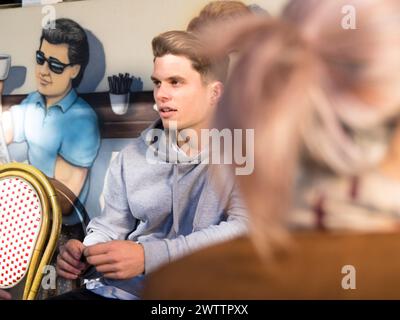 Junger Mann, der in einem Café neben einem Wandgemälde sitzt Stockfoto