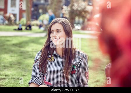Lächelnde junge Frau, die in einem sonnigen Park sitzt Stockfoto
