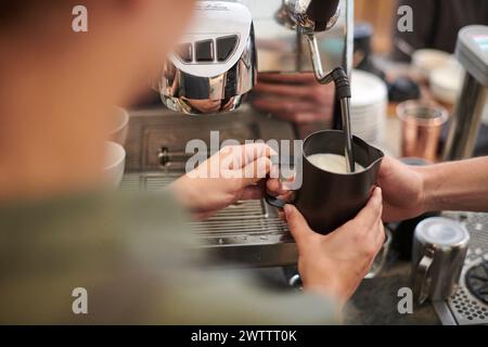 Der Barista schäumt Milch an einer Kaffeemaschine auf. Stockfoto