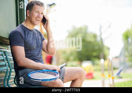 Mann, der am Telefon spricht, während er einen Tennisschläger hält. Stockfoto