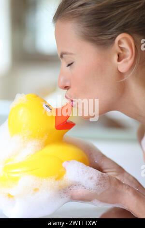 Frau küsst eine Gummiente in einem Schaumbad Stockfoto