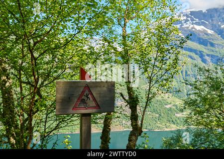 Gefahrenschild entlang des Wanderweges in Richtung des spektakulären Wasserfalls der Sieben Schwestern durch tiefgrünen Wald entlang des Geirangerfjords in Norwegen bei einer Sonne Stockfoto