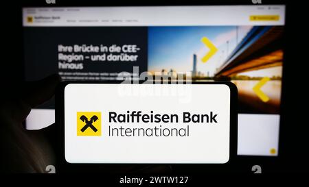 Person mit Mobiltelefon mit Logo der österreichischen Raiffeisen Bank International AG (RBI) vor der Webseite. Schwerpunkt auf dem Display des Telefons. Stockfoto