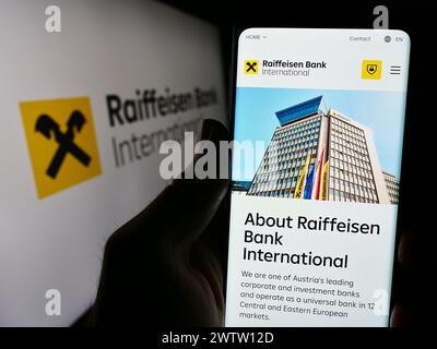 Handybesitzer mit Webseite der österreichischen Raiffeisen Bank International AG (RBI) mit Logo. Konzentrieren Sie sich auf die Mitte des Telefondisplays. Stockfoto
