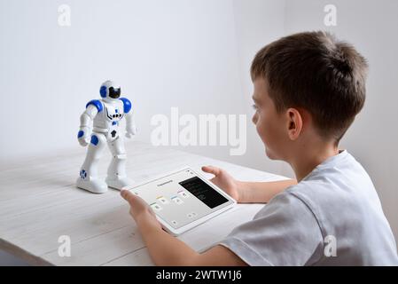 Junge programmiert die Arbeit eines Roboters auf einem Schreibtisch mit einem Tablet in der Hand Stockfoto