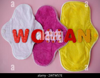 Drei abwaschbare Damenbinden aus Bambus mit der Aufschrift „WOMAN“. Bunte Öko-wiederverwendbare Menstruationspads auf rosa Hintergrund. Stockfoto