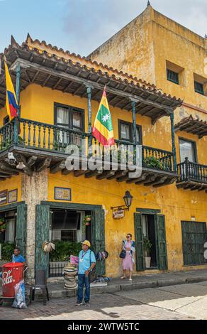 Cartagena, Kolumbien - 25. Juli 2023: El Pasquin Gastro Bar in Calle de las Carretas gelbe Fassade mit Holzbalkon mit Menschen und Coca-Cola Straße Stockfoto