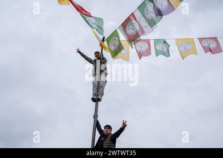 Batman, Türkei. März 2024. Zwei junge Menschen klettern mit den Fahnen auf den Pfosten und machen ein Siegeszeichen. Zehntausende von Menschen versammelten sich in Batman, um das neue Jahr und den Frühling mit großer Begeisterung und ihren farbenfrohen Kostümen zu feiern. (Foto: Bilal Seckin/SOPA Images/SIPA USA) Credit: SIPA USA/Alamy Live News Stockfoto