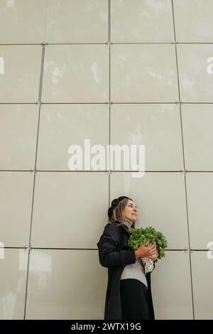 Eine Frau steht vor einer Wand und hält einen Haufen frisches Gemüse in der Hand. Vertikales Bild. Stockfoto