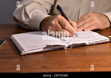 Ein Mann, der mit einem Füllfederhalter an einem Tisch sitzt, schreibt etwas auf die Blätter eines Notizbuchs. Stockfoto