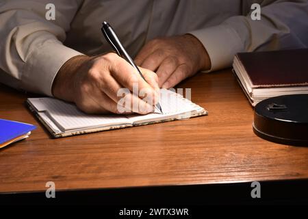 Das Bild zeigt einen Mann, der an einem Tisch sitzt und in ein Notizbuch schreibt. Stockfoto