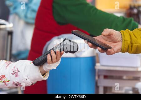 Leiche einer Frau in der Mitte, die ein Mobiltelefon hält und eine Online-Zahlung an einem Terminal tätigt, Nahaufnahme und Tiefwinkelansicht im Prager Street Food fa Stockfoto