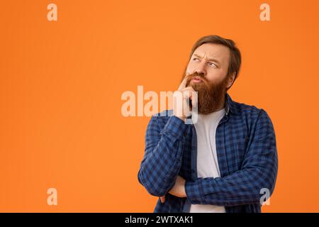 Rothaariger Mann in kariertem Hemd, der nachdenklich seinen Bart berührt, Studio Stockfoto
